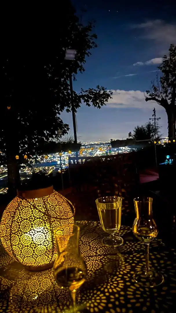 Orientalisches Windlicht und Gläser auf einem Terrassentisch, im Hintergrund die nächtlichen Lichter des Tals