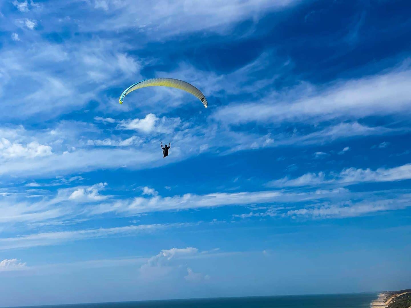 Gelbgrüner Gleitschirm vor blauem Himmel mit Schleierwolken über dem Meer