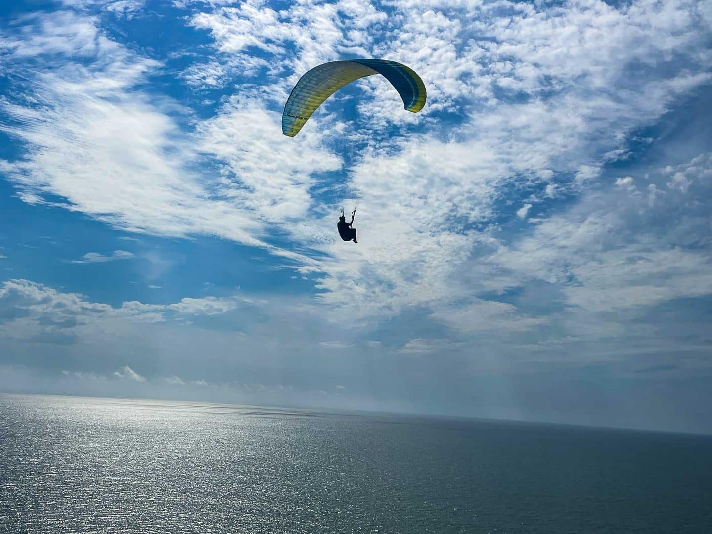 Gleitschirmflieger vor Schäfchenwolken, darunter das glitzernde Meer