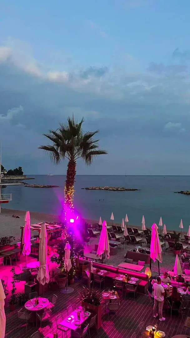 Strandbar mit Palme und pink beleuchteten Sonnenschirmen am Meer in der Abenddämmerung