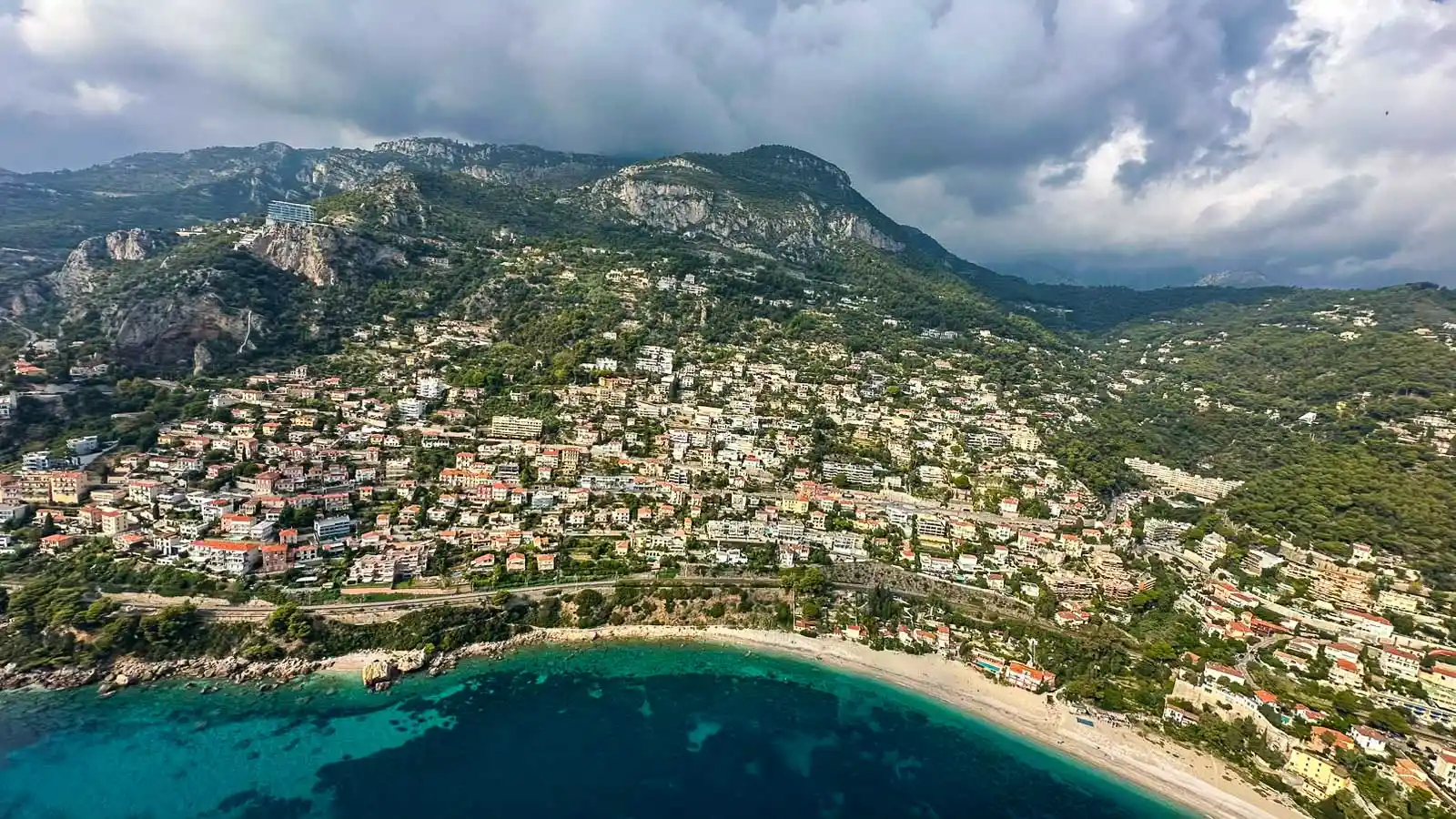 Luftaufnahme von Roquebrune-Cap-Martin mit Bucht, türkisem Meer und Bergen der Seealpen