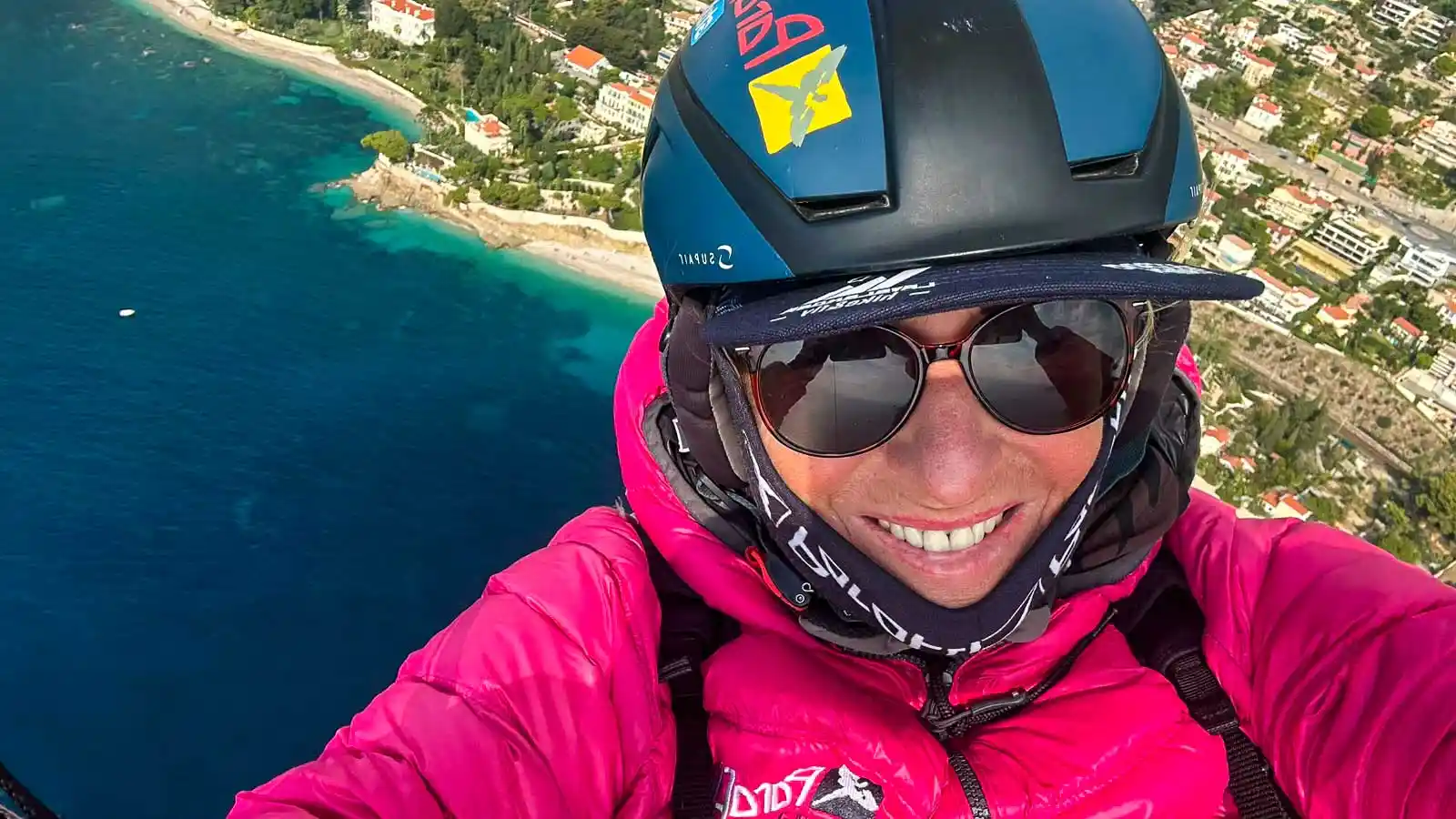 Lächelnde Pilotin mit Helm und Sonnenbrille macht ein Selfie im Flug über der Küste